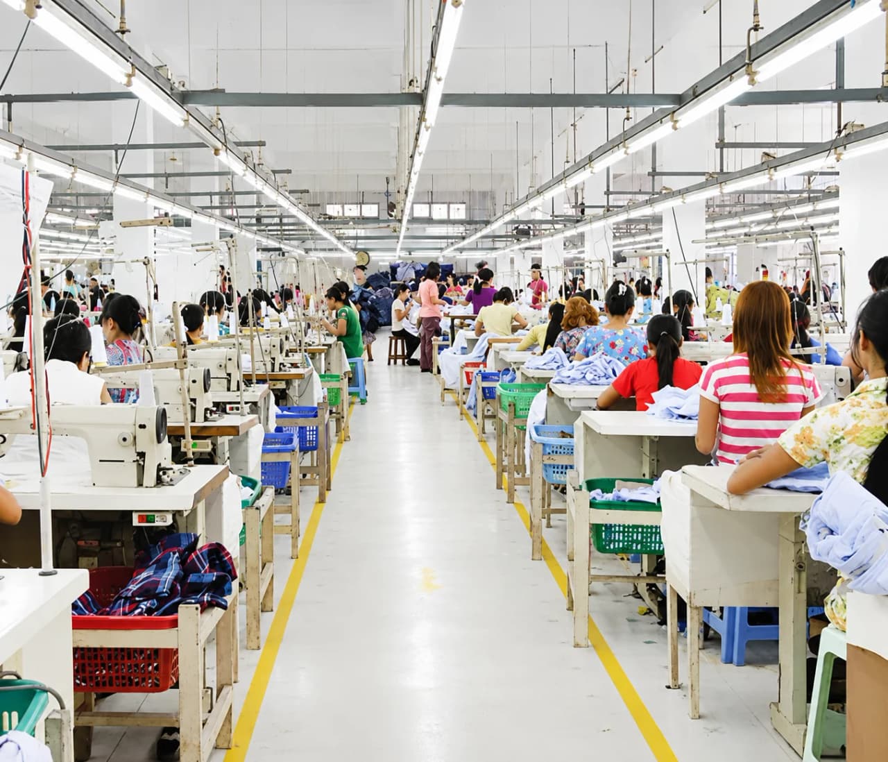 Bright production workshop with workers at rows of industrial sewing machines
